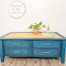A coffee table with drawers refurbished by Revival of the Thriftest is painted with Dixie Belle's Antebellum Blue chalk mineral paint and has a natural wood table top inlay.