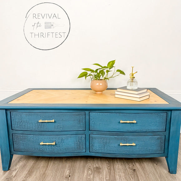 A coffee table with drawers refurbished by Revival of the Thriftest is painted with Dixie Belle's Antebellum Blue chalk mineral paint and has a natural wood table top inlay.