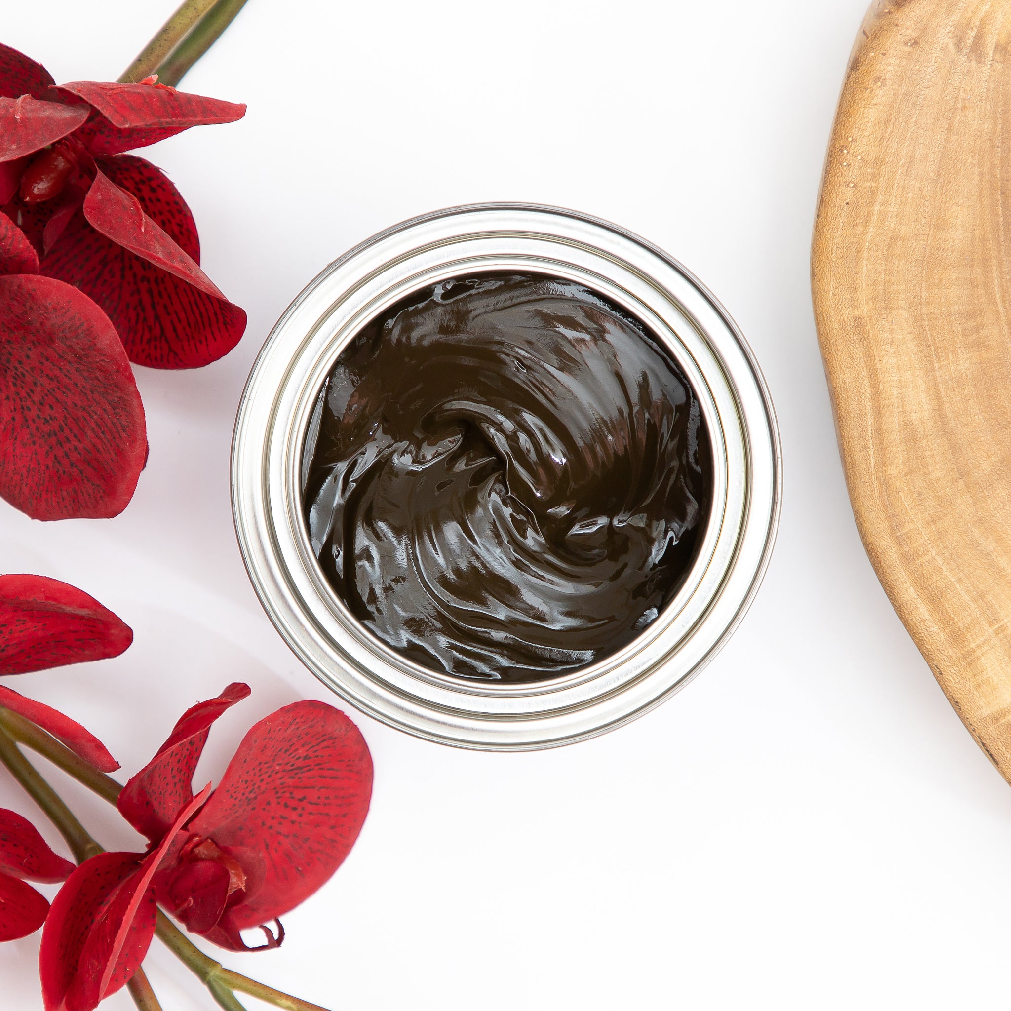 A arial view of an open can of Dixie Belle's No Pain Gel Stain is against a white background. To the left of the can is red silk flowers.