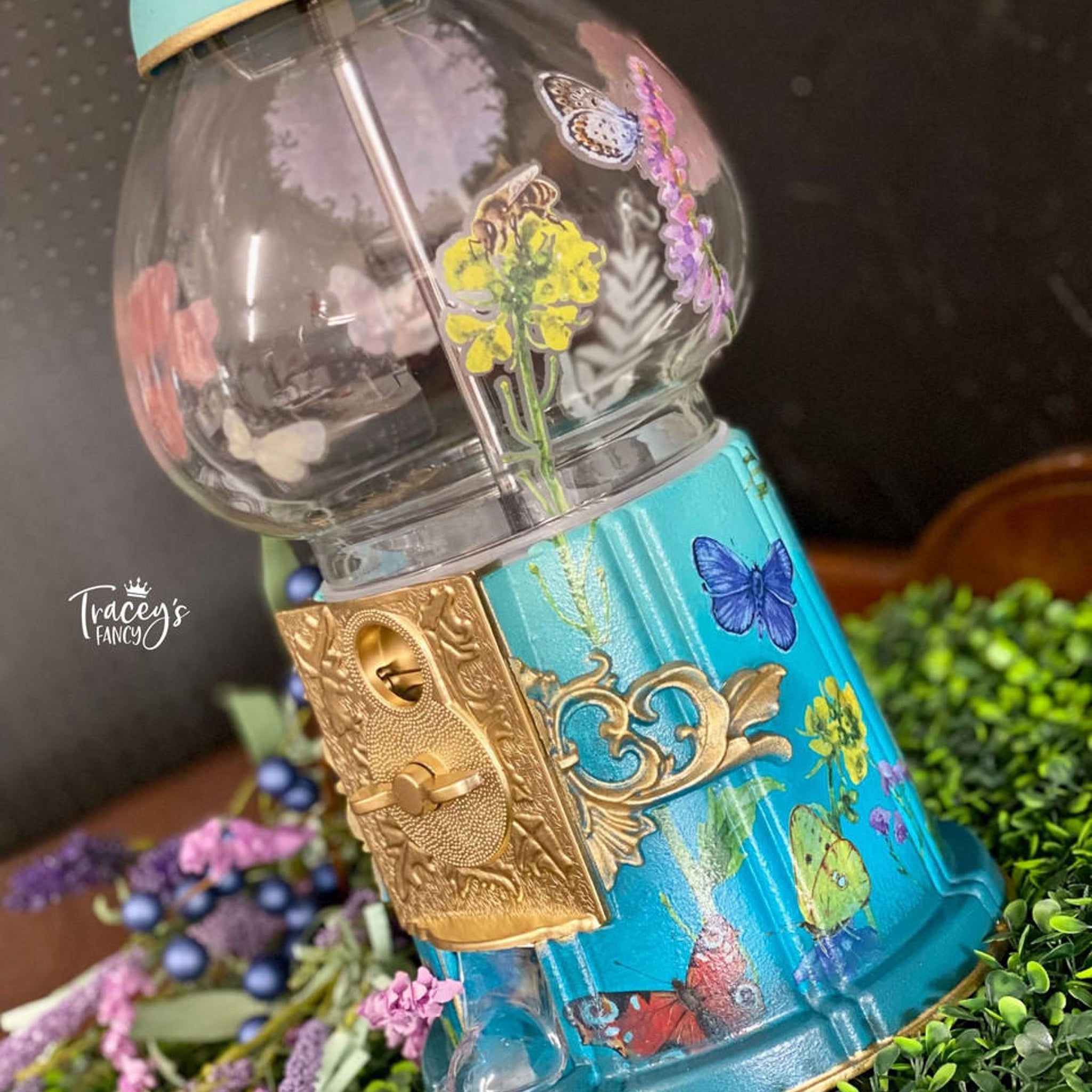 A gumball machine refurbished by Tracey's Fancy is painted teal blue and features the Wildflowers & Butterflies transfer on it.