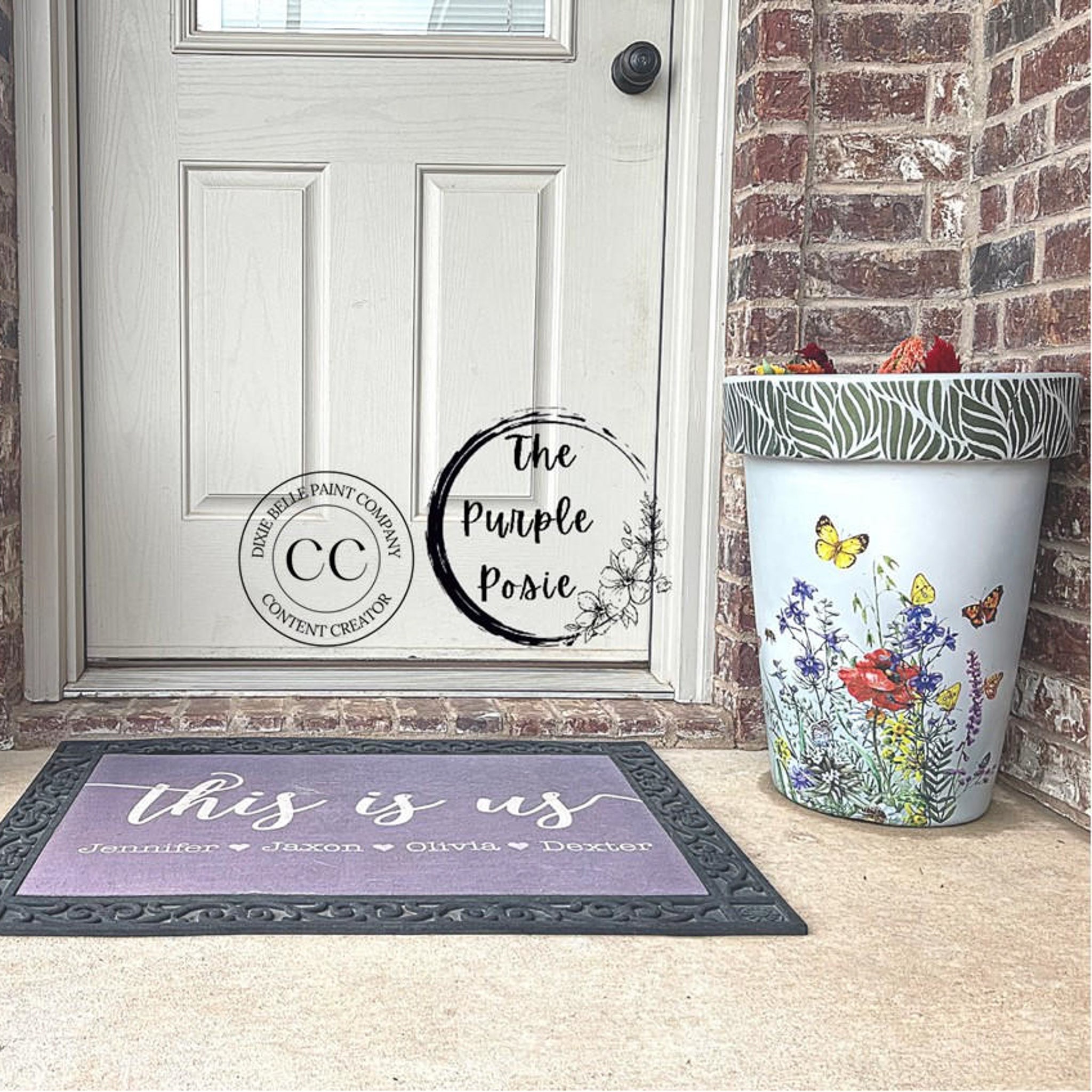 A vintage side drum table refurbished by The Purple Posie, a Dixie Belle Paint Company Content Creator, is sitting on a porch next to a front door and is painted white and features the Wildflowers & Butterflies Transfer on it.