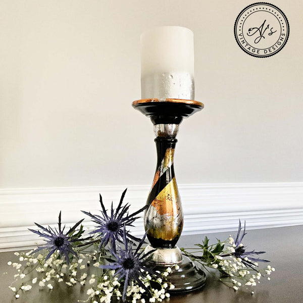 A vintage candle holder refurbished by Aj's Vintage Designs is painted black and features Dixie Shine foil in copper, silver, and gold. Loose flowers sit around the base of the candle holder.