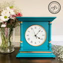 A vintage table clock refurbished by Aj's Vintage Designs is painted a teal blue with Dixie Shine gold foil accents. A glass vase with small wildflowers sits to the left of the clock.