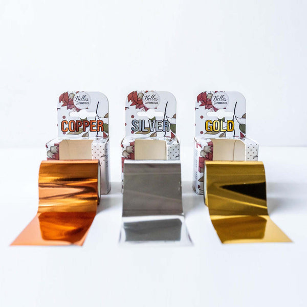 Three packages of Dixie Shine foil rolls featuring copper, silver, and gold are displayed on a white background. The rolls of foil are displayed in front of the packages.