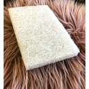 A rectangular white finishing pad is sitting on a mauve colored, long, faux fur piece of carpet.