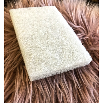 A rectangular white finishing pad is sitting on a mauve colored, long, faux fur piece of carpet.