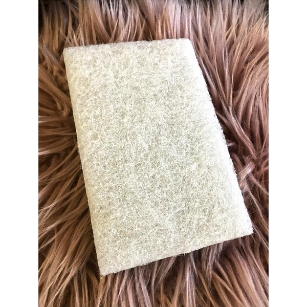 A rectangular white finishing pad is sitting on a mauve colored, long, faux fur piece of carpet.