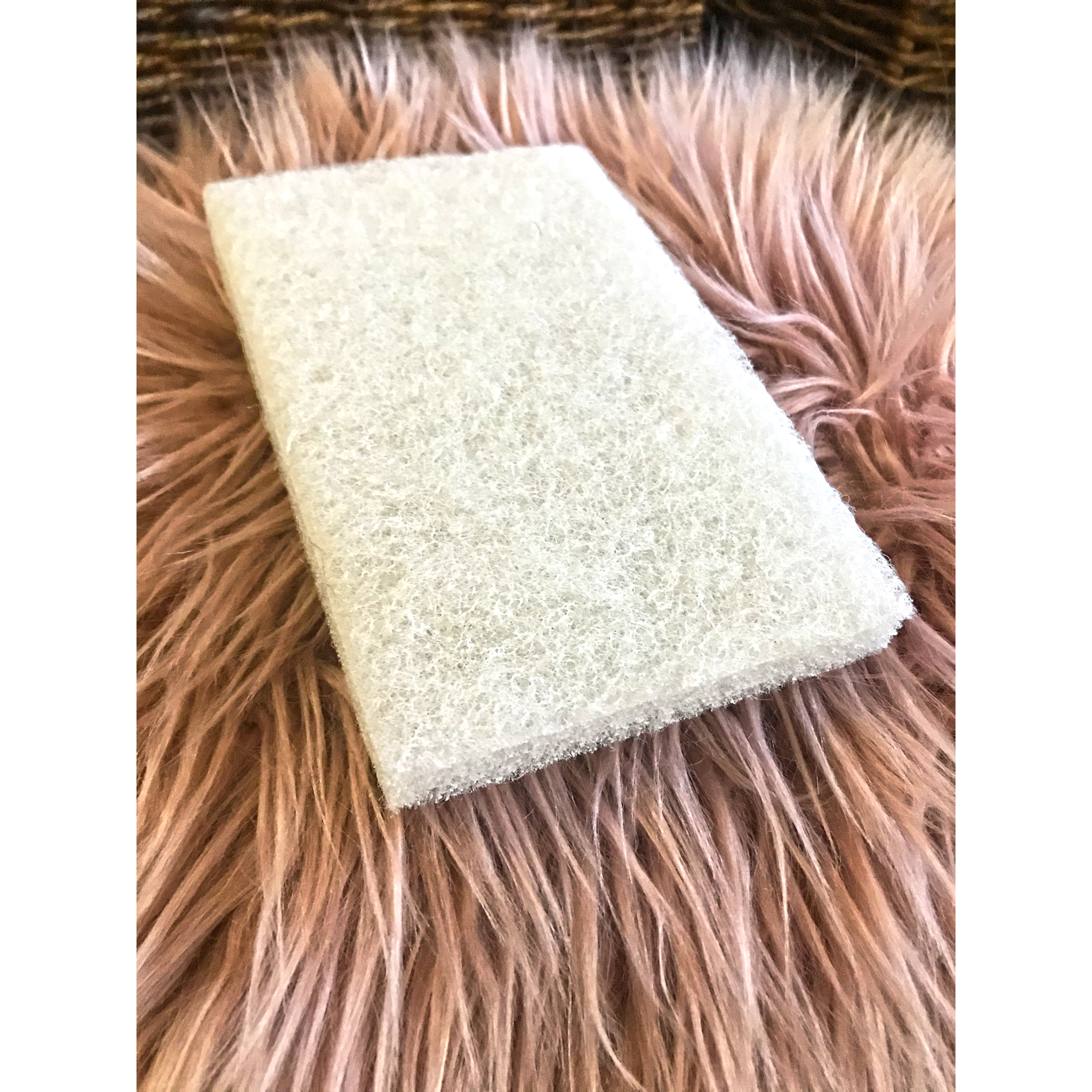 A rectangular white finishing pad is sitting on a mauve colored, long, faux fur piece of carpet.