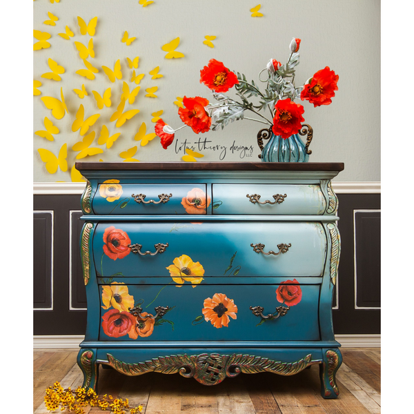 A vintage Bombay style dresser refurbished by Lotus Theory Designs is painted a blend of blue and pale blue with bronze accents and features ReDesign with Prima's Poppy Garden transfer on its drawers.