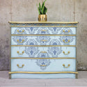 A 4-drawer dresser refurbished by Kacha is painted light blue with gold accents and features the Kacha Dana Damask transfer on it.