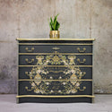 A dresser refurbished by Kacha is painted black with gold accents and features the Kacha Petite A Petite transfer on its drawers.