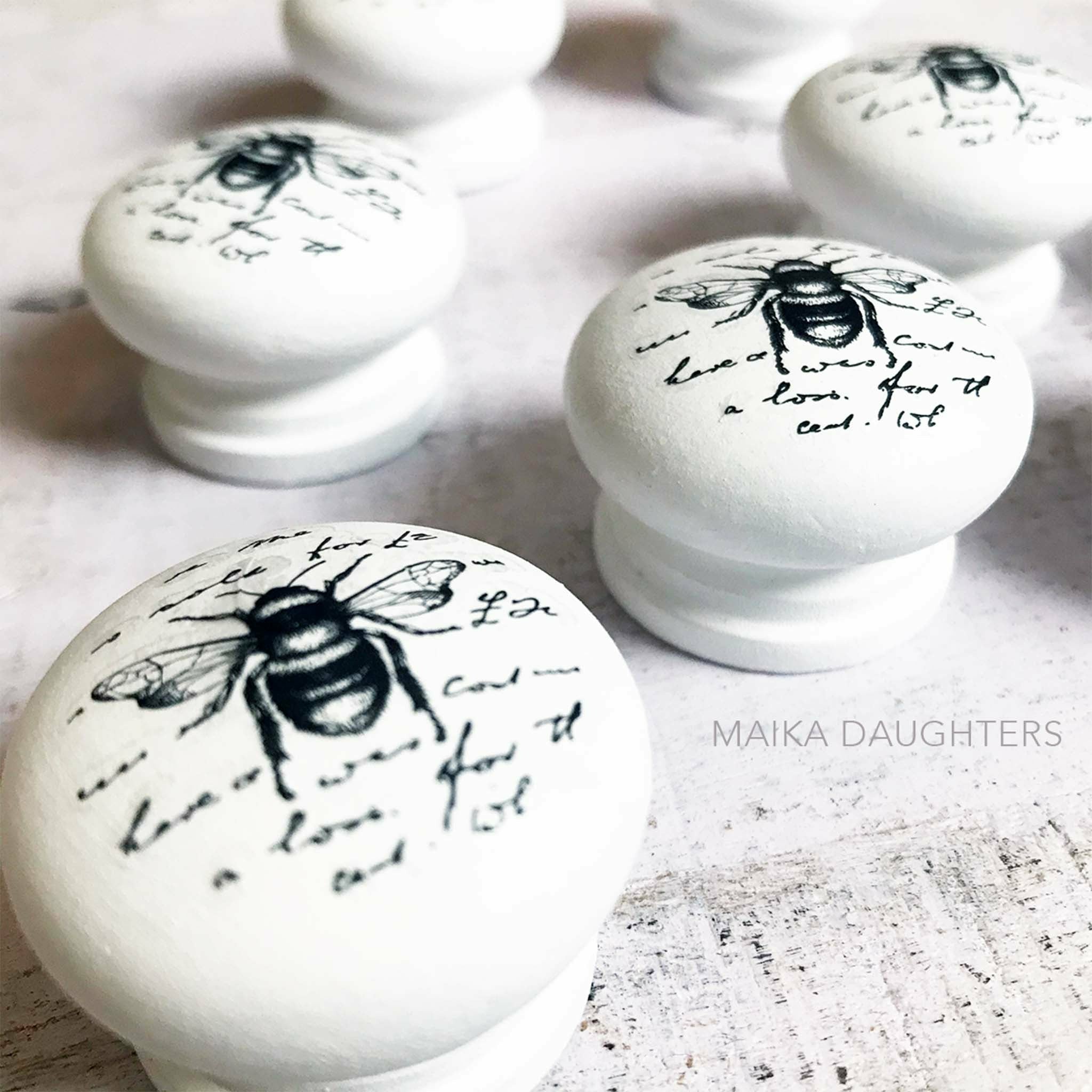 White knobs with the Paris Cottage transfers on top. A gray Maika Daughters logo on the right.