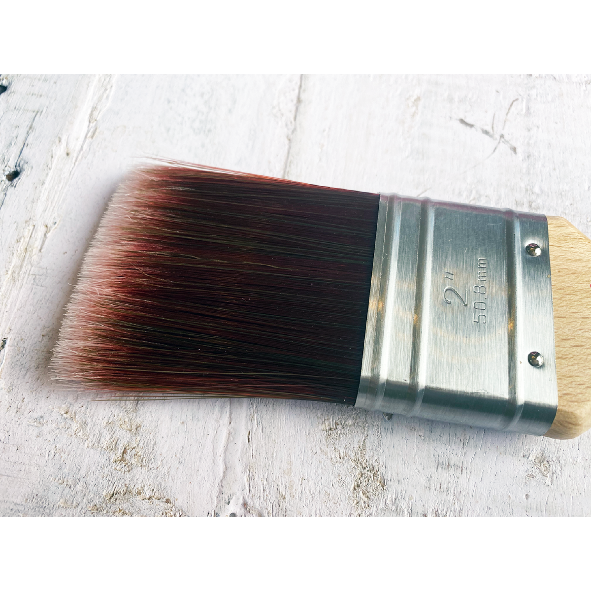Close-up view of Dixie Belle Paint Company's Mini Synthetic Paint Brush against a white wood background. White borders are on the top and bottom.