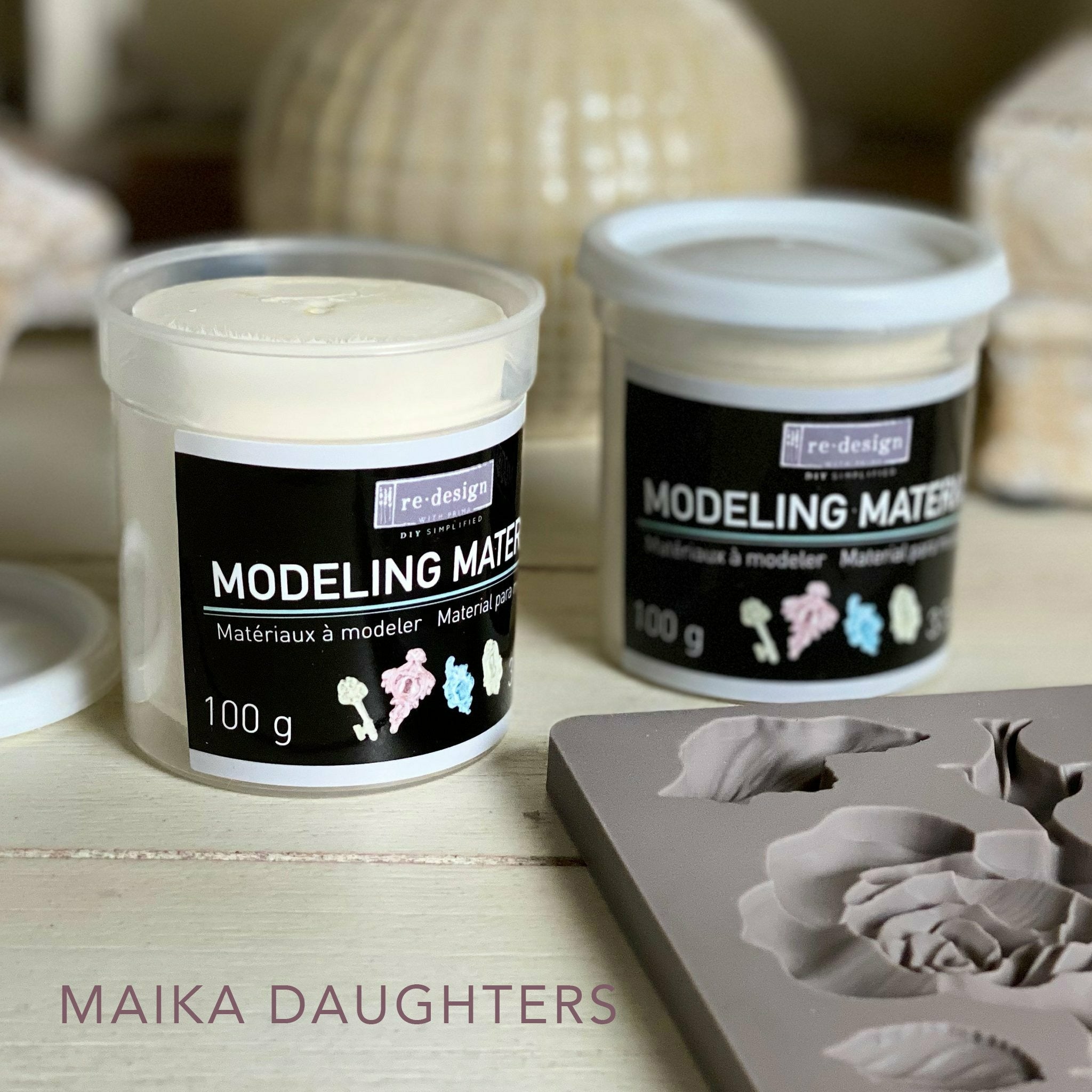 One open and one closed air dry modeling material containers reading: Redesign with prima. Modeling Material. Materiaux a modeler. Material para modelar. 100 g. 3.5 oz. A mauve Maika Daughters logo on the bottom left.