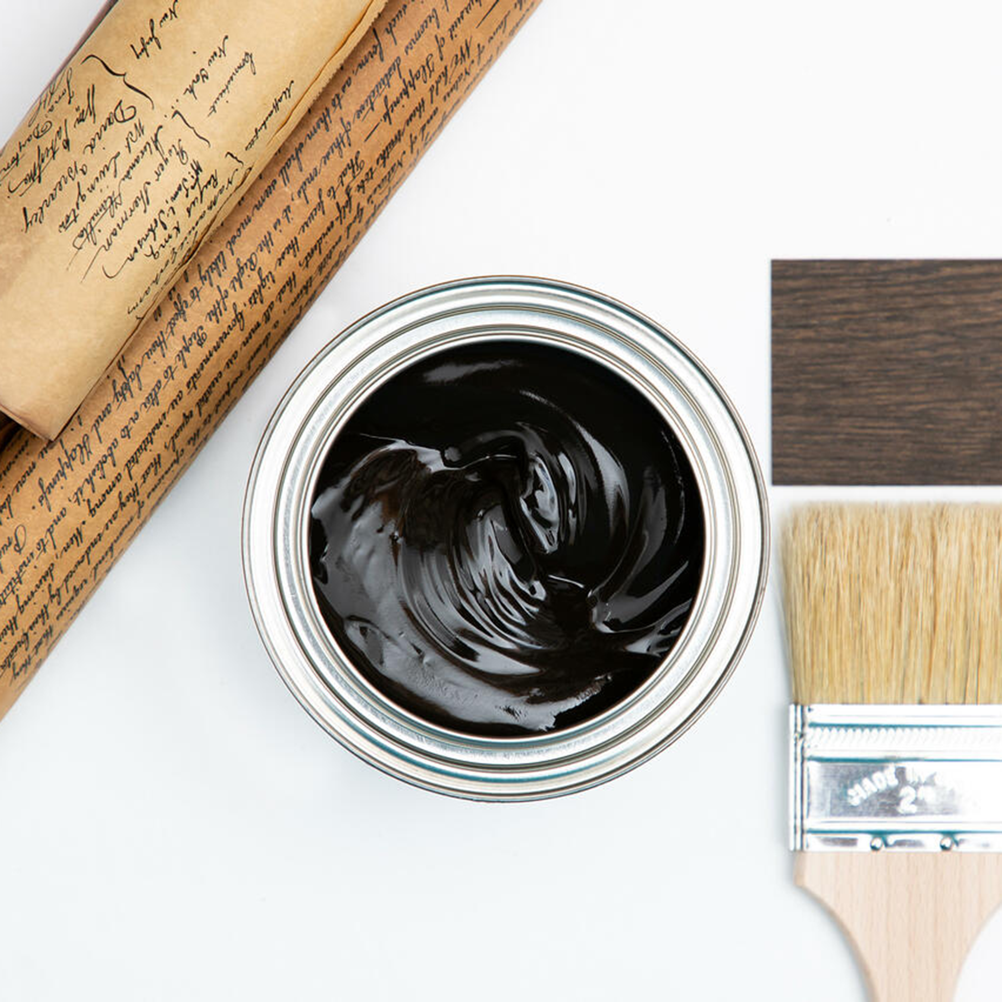 A arial view of an open can of Dixie Belle's No Pain Gel Stain in Walnut is against a white background. The can is surrounded by a paint brush, a parchment scroll, and a wood swatch featuring the stain color.