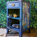 A vintage nightstand refurbished by The Grandson's Brush is painted blue and features the Cosmic Roses transfer on it.
