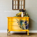 A vintage dresser refurbished by Leah Noell Design Co. is painted mustard yellow and features the Cosmic Roses transfer on its drawers.