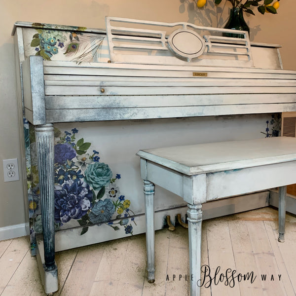 A vintage piano refurbished by Apple Blossom Way is painted white and features the Cosmic Roses transfer on it.