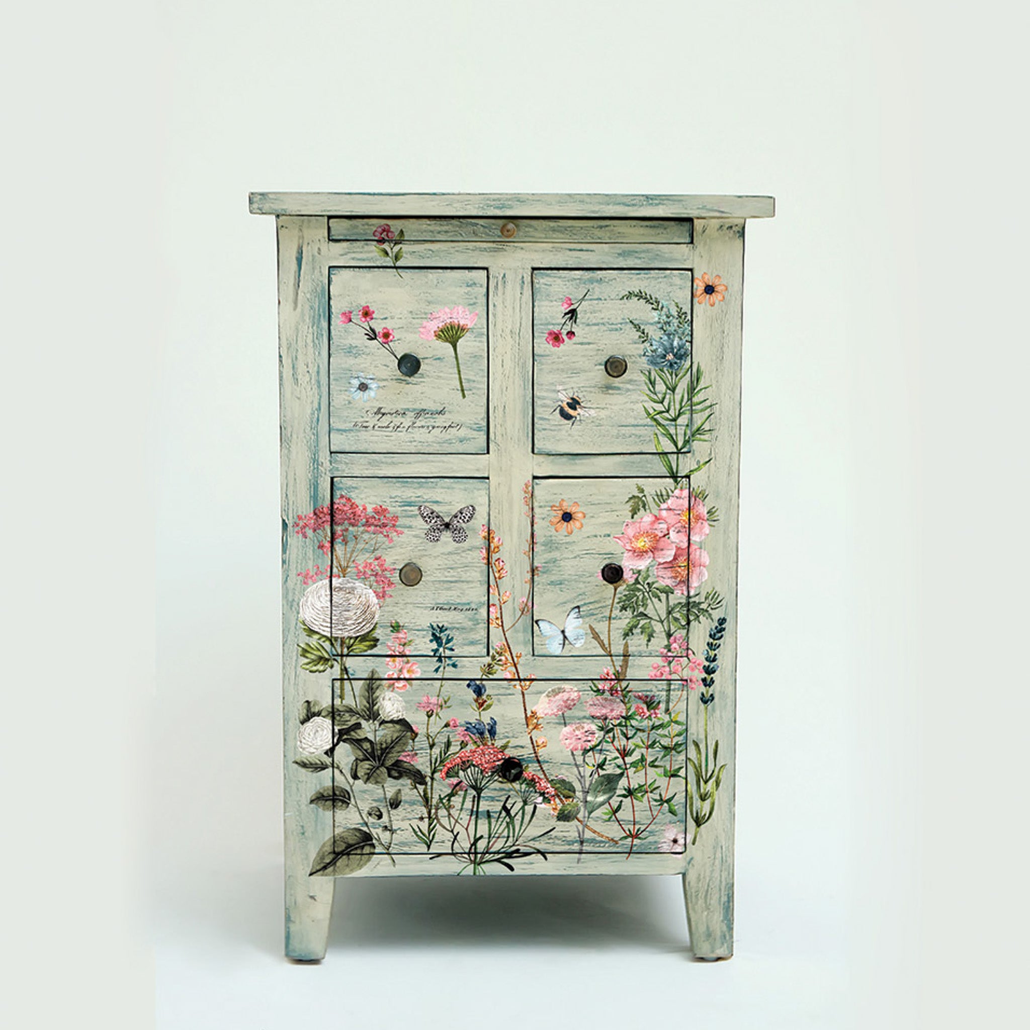 A small vintage nightstand with storage is painted cream with hints of blue weathering and features ReDesign with Prima's Botanical Paradise small rub-on transfer.