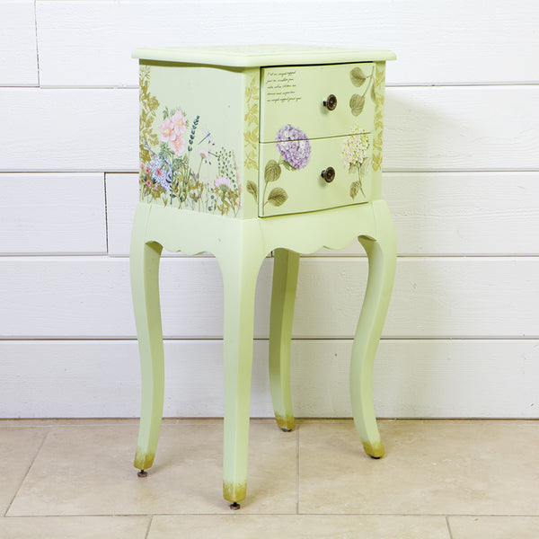 A small vintage 2-drawer nightstand is painted light green and features the Botanical Paradise transfer on it.
