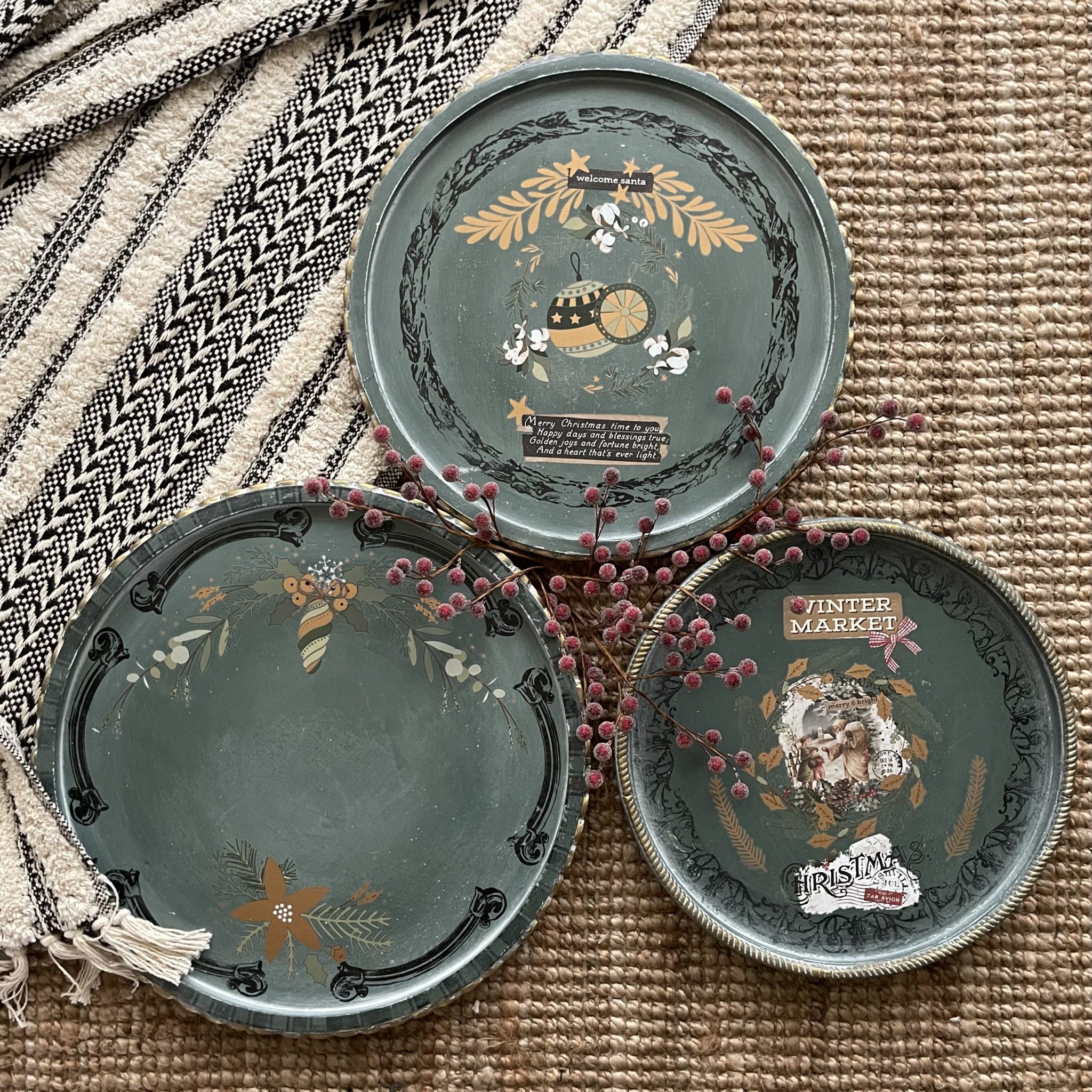 Three coaster style candle plates are painted a muted green and feature ReDesign with Prima's Holiday Spirit small transfer on them.