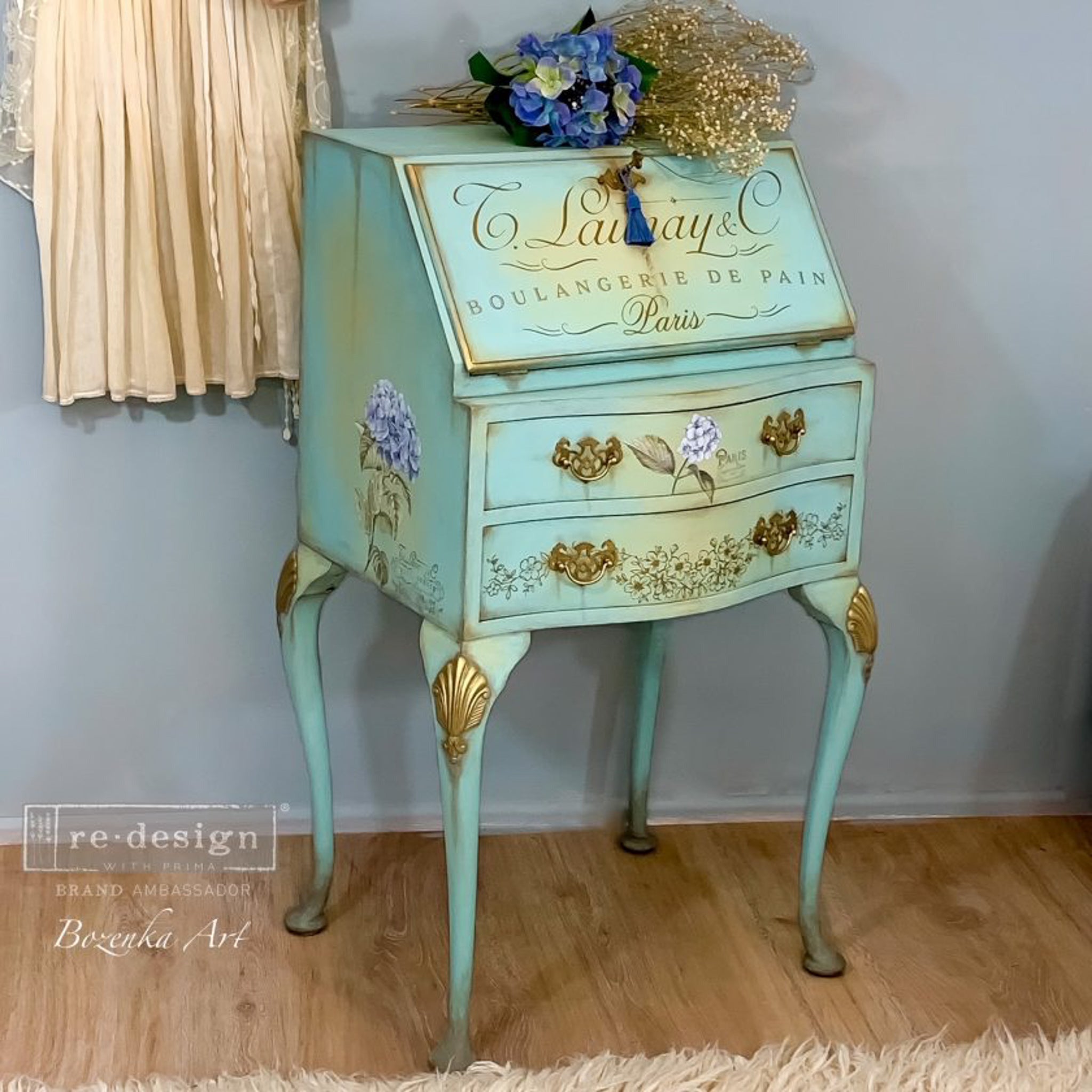 A vintage secretary's desk refurbished by Bozenka Art is painted a blend of light teal and yellow with gold accents and features ReDesign with Prima's Mystic Hydrangea small transfer on it.