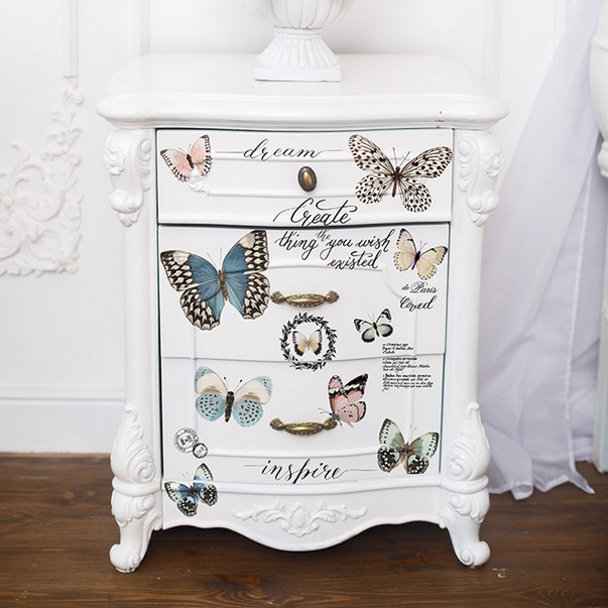 A vintage night stand is painted white and features ReDesign with Prima's Papillon small transfer on its door and drawer.