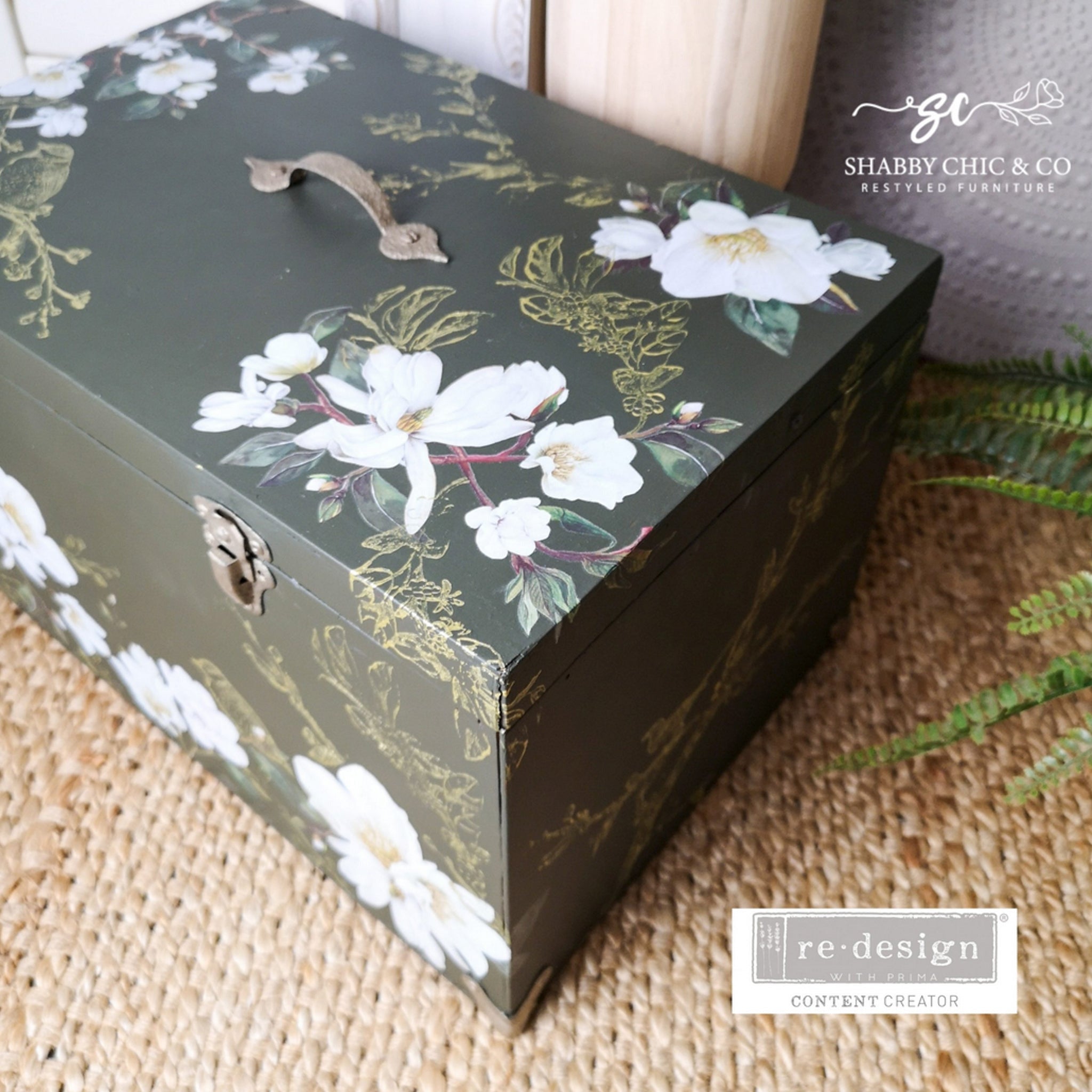 An arial corner view of a vintage footlocker storage chest refurbished by Shabby Chic & Co. Restyled Furniture is painted hunter green and features ReDesign with Prima's White Magnolia small transfer on it.