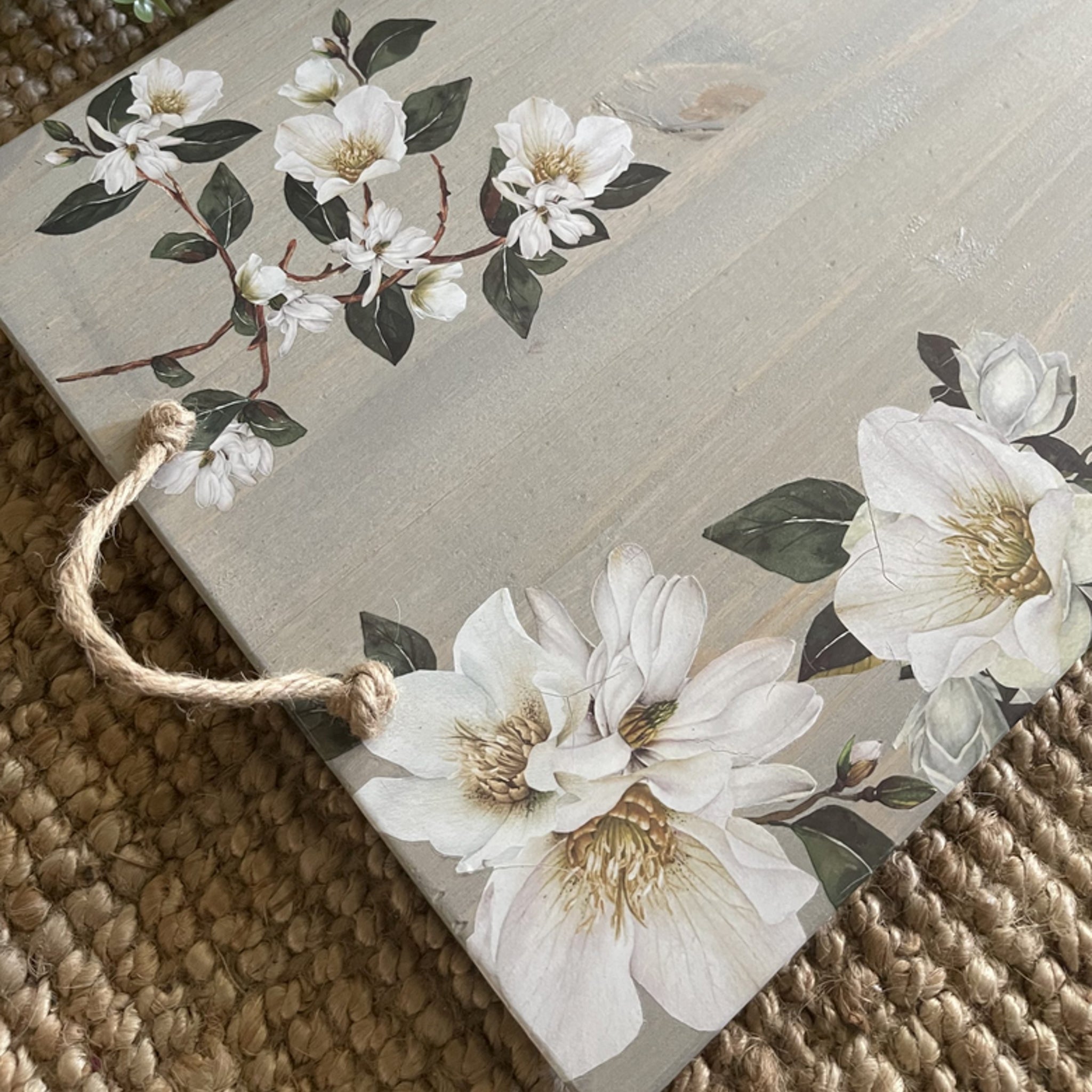 A close-up of a wood serving tray with a rope handle is white-washed and features ReDesign with Prima's White Magnolia small transfer on it.