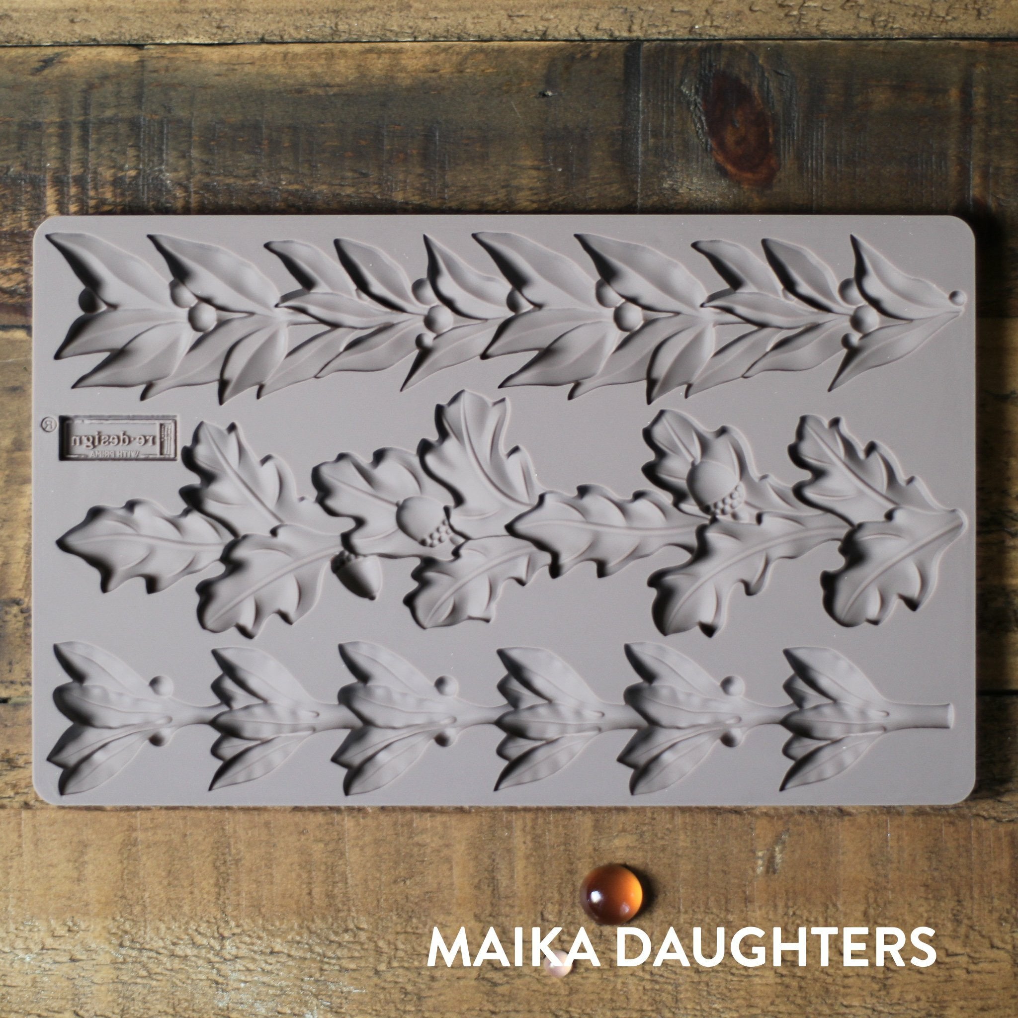 Wooden background with the Louelle Borders mold tray on top. A white Maika Daughters logo is in the bottom right corner.