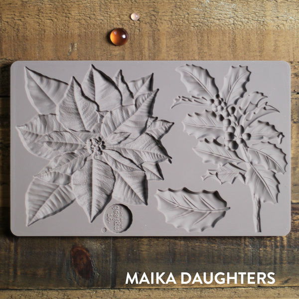 Wooden background with the Perfect Poinsettia mold tray on top. A white Maika Daughters logo in the bottom right corner.
