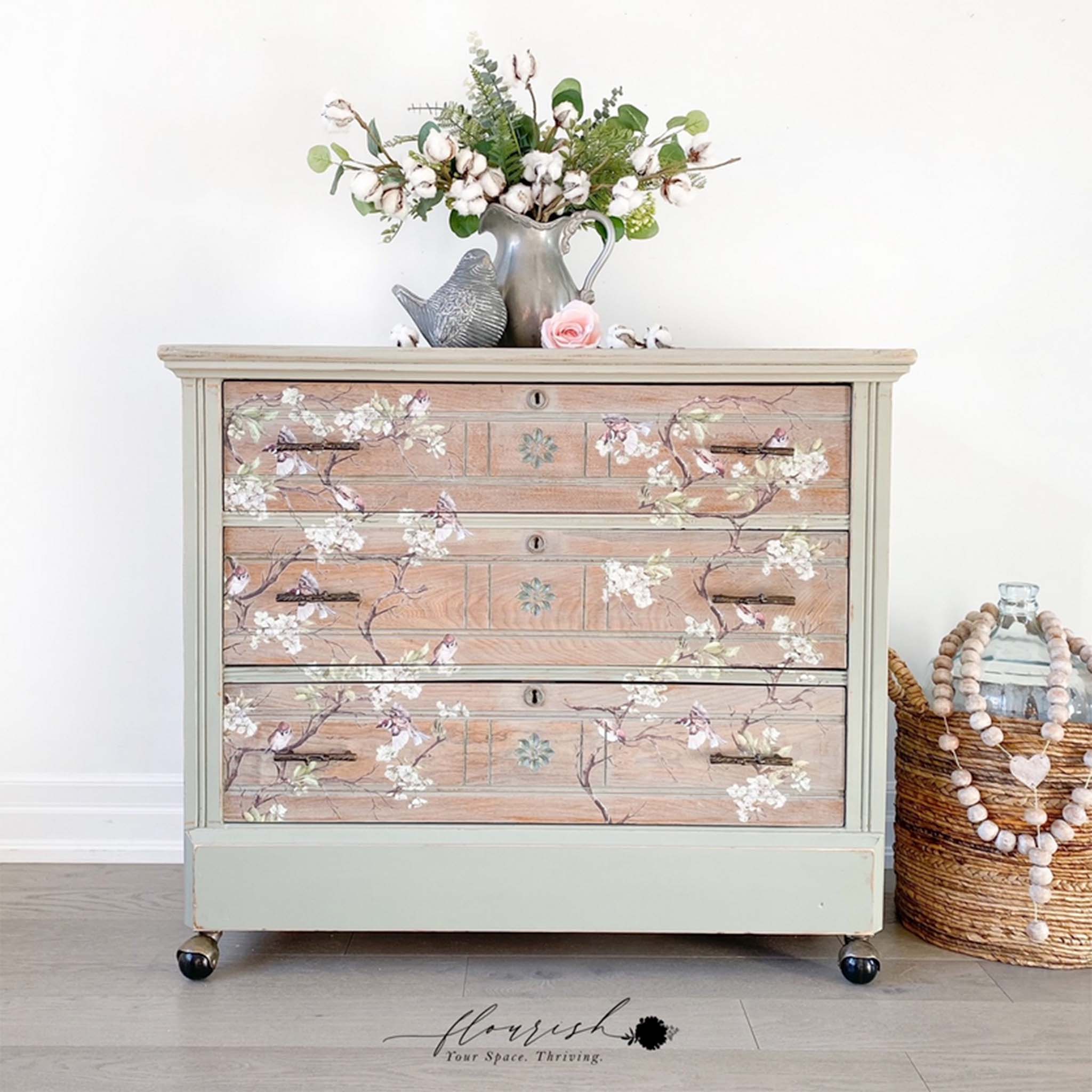 Tan dresser with the Blossom Flight transfer on top. A black Flourish your space thriving logo on the bottom right.