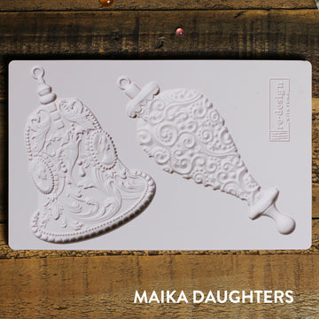 Wooden background with a mold of two bells and a redesign logo in the top right corner.  A white maika daughters logo is in the bottom right corner.