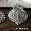 Wooden background with a close up of the victorian adornments castings painted in a metallic silver. A white Maika Daughters logo is sat in the bottom right corner.
