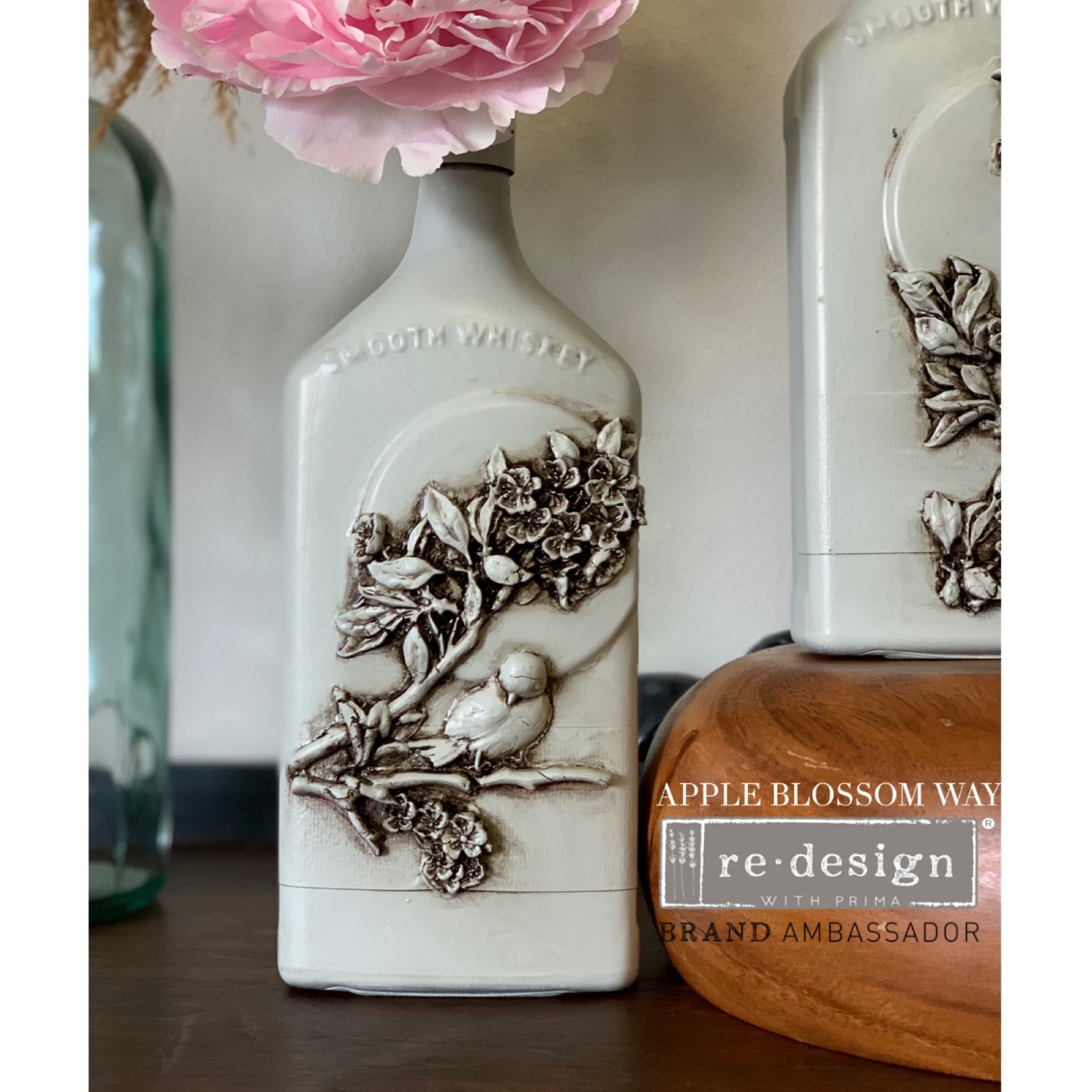 A vintage smooth whiskey bottle refurbished by Apple Blossom Way, a ReDesign with Prima Brand Ambassador, is painted white and features the Aviary silicon mould on it.
