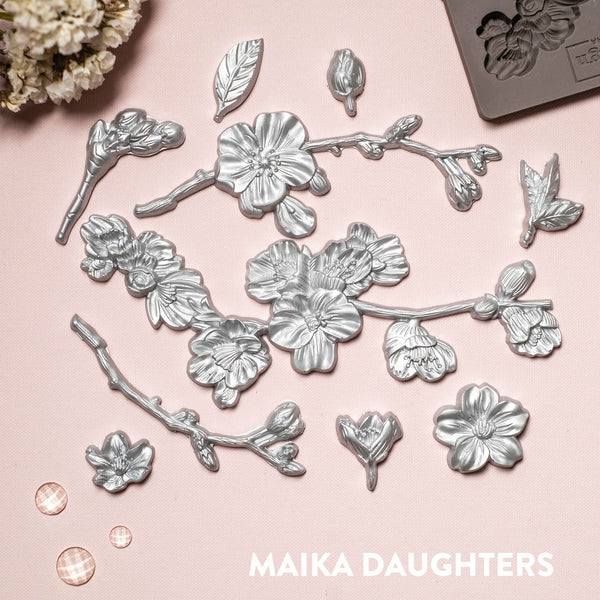Silver colored castings of ReDesign with Prima's Cherry Blossoms silicone mould is against a light pink background.