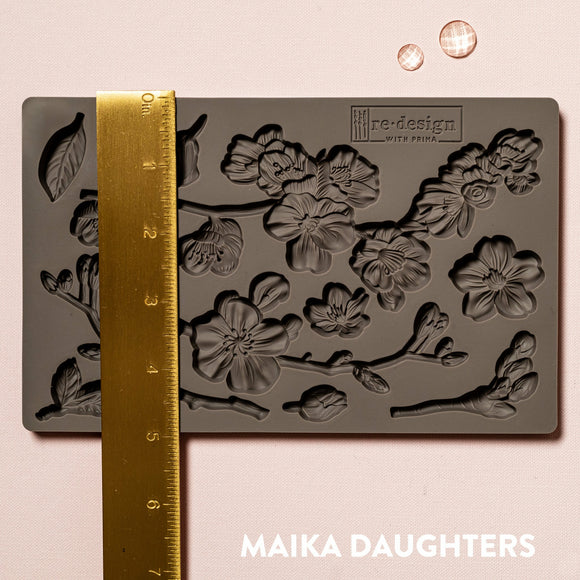 A brown silicone mould of ReDesign with Prima's Cherry Blossoms is against a light pink background. A gold ruler reading 5 inches sits on the mould.