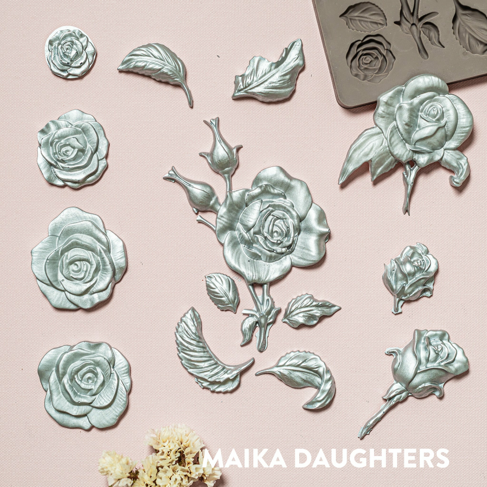 Silver colored silicone castings of rose blooms and leaves are against a light pink background.