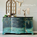 A vintage dresser refurbishd by Leah Noell Design Co. is painted a blend of blue greens and features the Golden Emblem silicone mould castings on it.