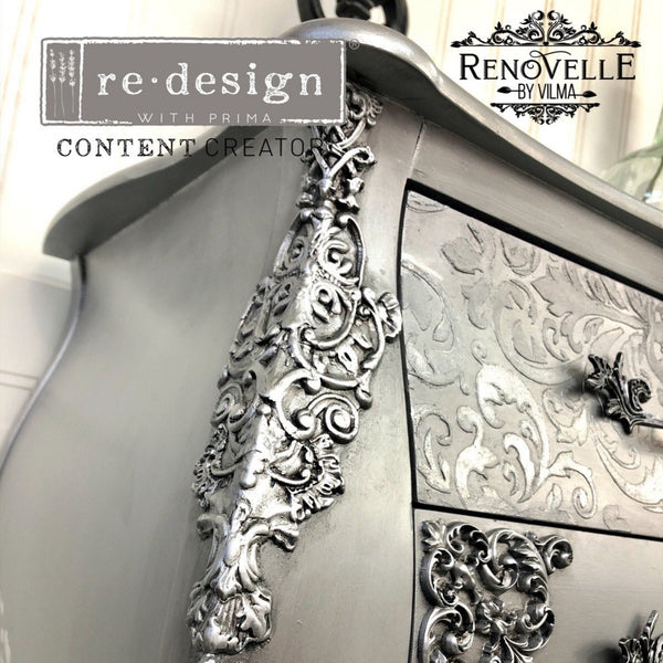A close-up of a vintage 3-drawer dresser refurbished by Renovelle by Vilma is painted silver and features the Golden Emblem silicone mould castings on it.