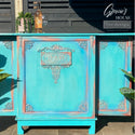 A vintage bar cabinet refurbished by Gracie's House is painted bright blue and features the Golden Emblem silicone mould castings on it.