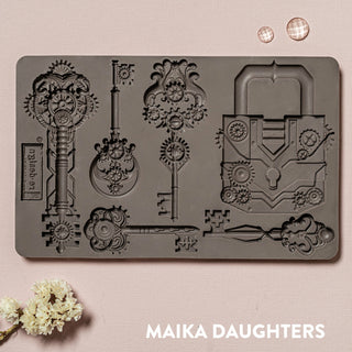 A brown silicone mould of ReDesign with Prima's Mechanical Lock & Keys is against a light pink background.