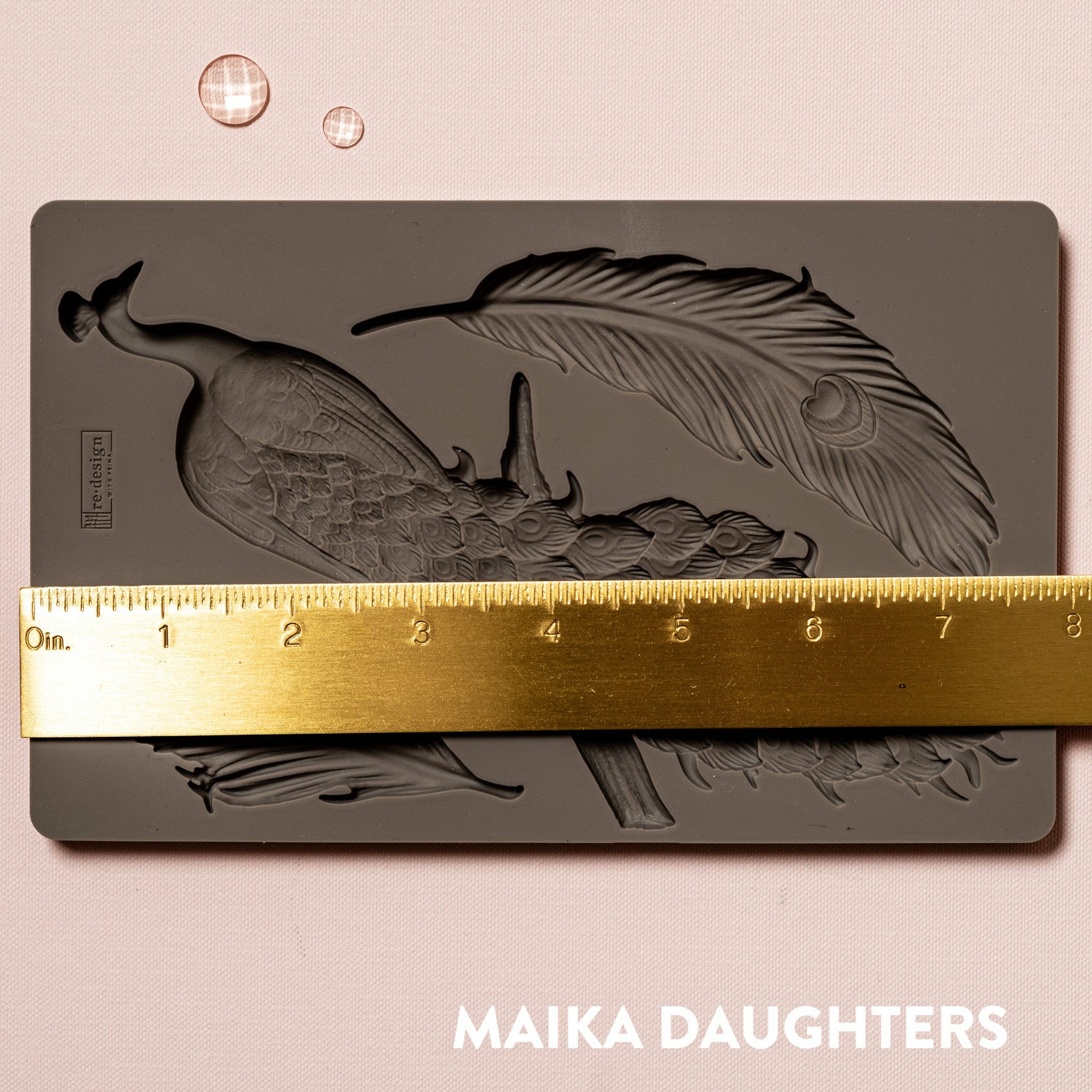 A brown silicone mould of ReDesign with Prima's Regal Peacock is against a light pink background. A gold ruler reading 8 inches sits on the mould.