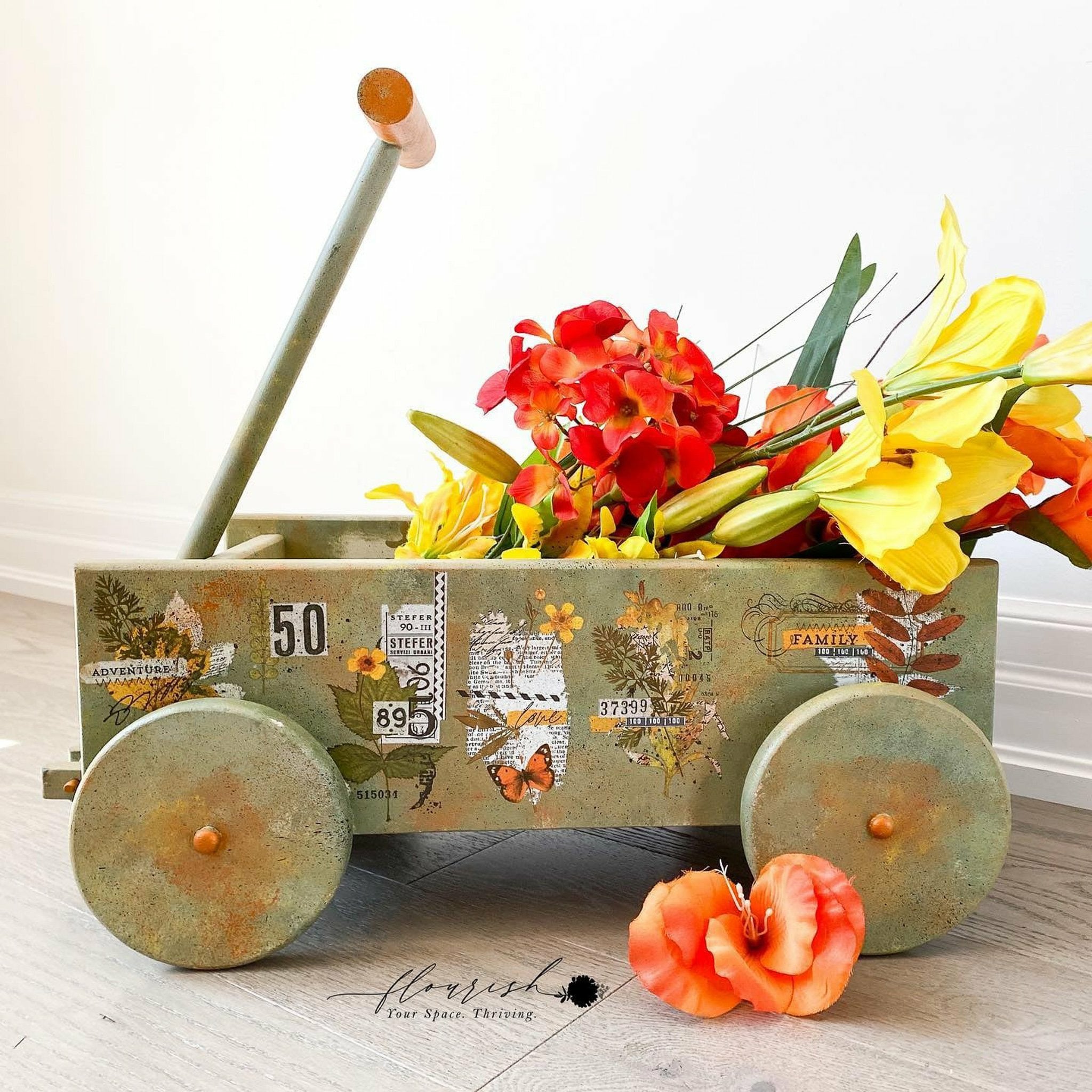 A small decor wagon filled with flowers and the Autumn Essentials transfer on top. A black logo reading: Flourish Your space. Thriving. on the bottom.