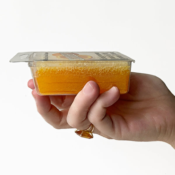 A side view of Orange Scrubby Soap is being held in a hand.