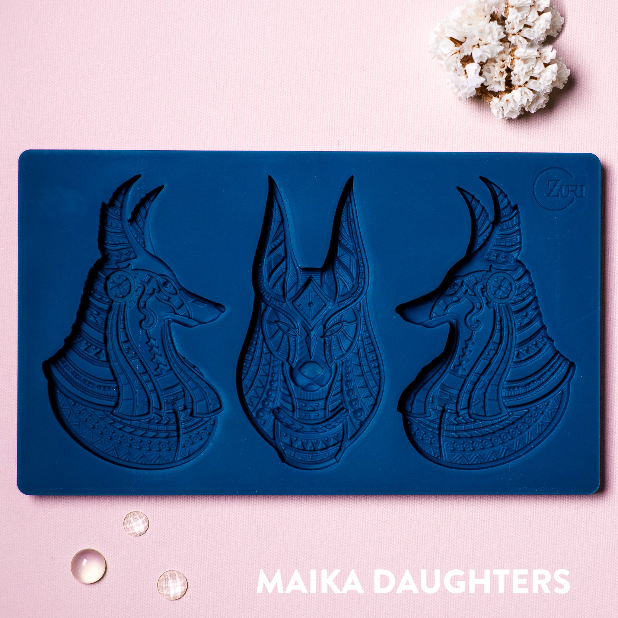 A blue silicone mold of Zuri's Anubis Heads is on a light pink background.