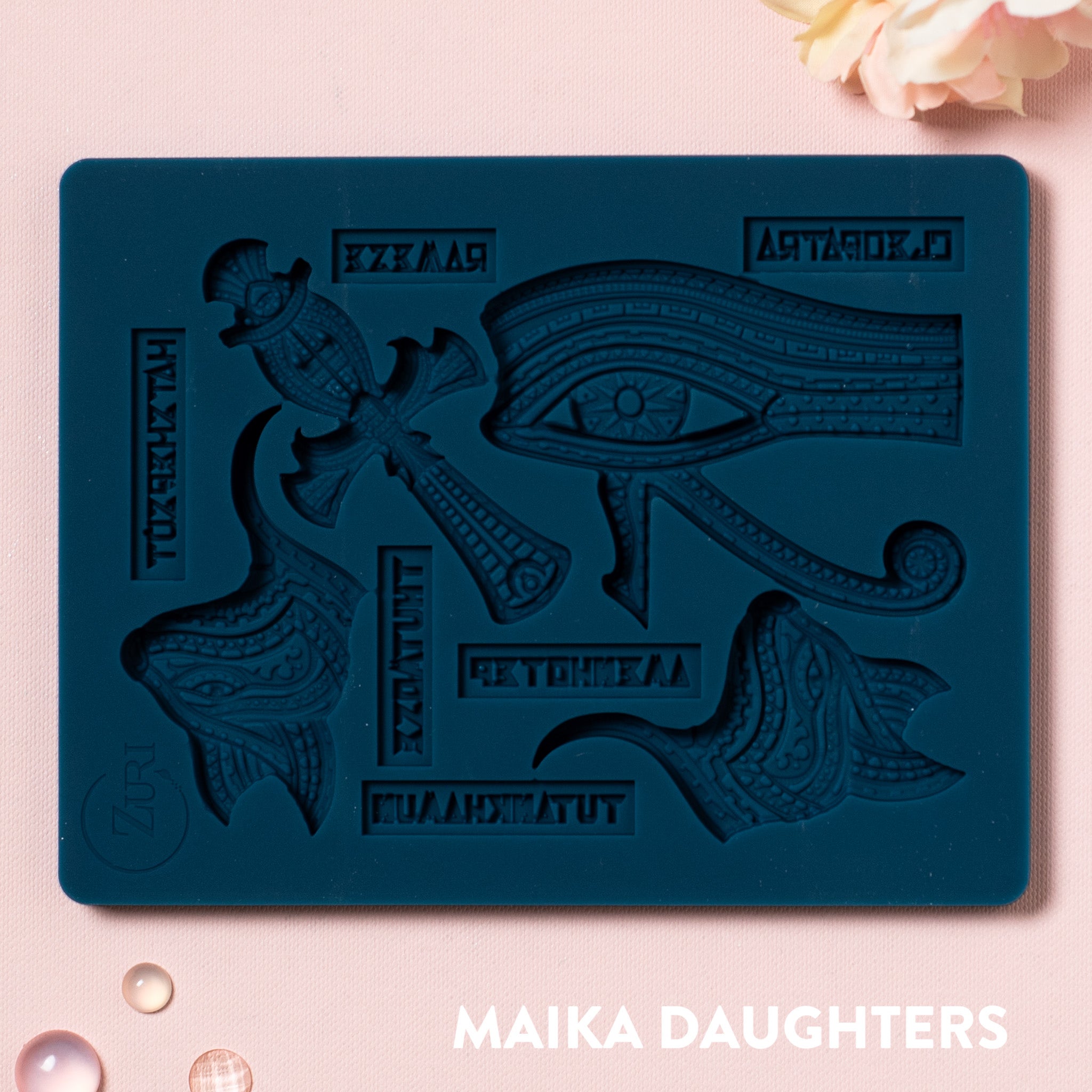 A blue silicone mold of Zuri's Eyptian Motifs is on a light pink background.